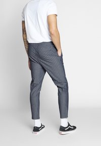 Szare spodnie w paski o luźnym kroju, z elastycznym pasem i bocznymi kieszeniami, zestawione z czarnymi trampkami i białymi skarpetkami.