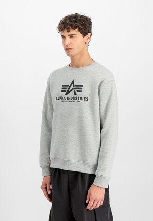 Siv sweatshirt z črnim logotipom "ALPHA INDUSTRIES." Ima rebrast rokav in rob, sproščen kroj ter mehak, teksturiran material.