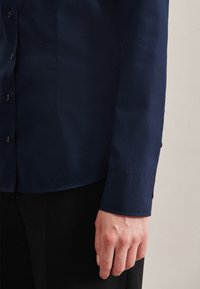 Camicia a maniche lunghe blu navy con una texture liscia, polsini con bottoni e una vestibilità sagomata. Presenta cuciture sottili e un colletto classico.