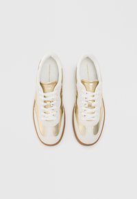 Adidași albaștri și aurii cu un superior din piele netedă, accente din suede texturat, șireturi plate albe și o talpă din cauciuc.