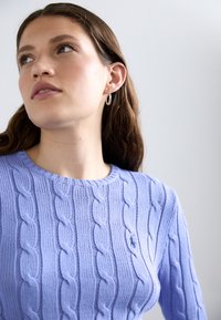 Maglione lavorato a maglia color lilla chiaro con scollo rotondo e maniche lunghe; presenta un motivo testurizzato e un piccolo logo in evidenza sul petto.