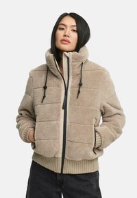 Beige fleecejack met gewatteerde textuur, hoge kraag, ritssluiting en verstelbare koordjes. Ribgebreide manchetten en zoom. Lichtgewicht en casual.