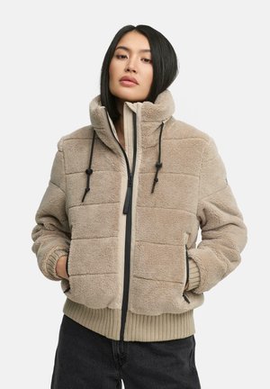 Veste en polaire beige avec texture matelassée, col haut, fermeture éclair et cordons de serrage ajustables. Poignets et ourlet côtelés. Légère et décontractée.