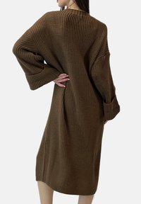 Bruine gebreide jurk met een losse pasvorm, lange mouwen, geribbelde textuur en een lengte tot halverwege de kuit, met zijslitten voor meer bewegingsvrijheid.