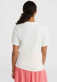 Hvid bomulds T-shirt med korte ærmer og rund halsudskæring, vist med en lyserød nederdel, set fra ryggen. Glat tekstur.