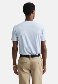 Lichtblauw T-shirt met een ontspannen pasvorm, korte mouwen en een ronde hals, gecombineerd met zandkleurige broek en een zwarte riem. Eenvoudig ontwerp, geen patronen.