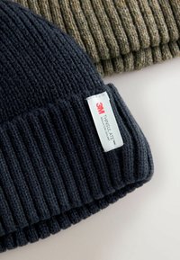Czarna, prążkowana czapka zakrywająca uszy z białą metką z napisem "3M THINSULATE". Tekstura jest miękka, odpowiednia do zapewnienia ciepła w chłodne dni.