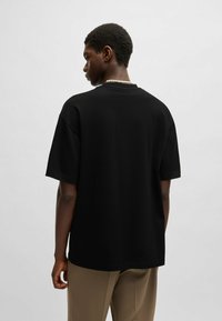 Black cotton T-shirt with short sleeves, relaxed fit, and a crew neckline. Worn with beige trousers, showcasing a simple, minimal design.