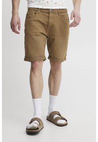 Beige Denim-Shorts mit umgeschlagenen Säumen, fünf Taschen und vorderem Knopfverschluss, kombiniert mit weißen Socken und braunen Sandalen. Minimalistisches Design.