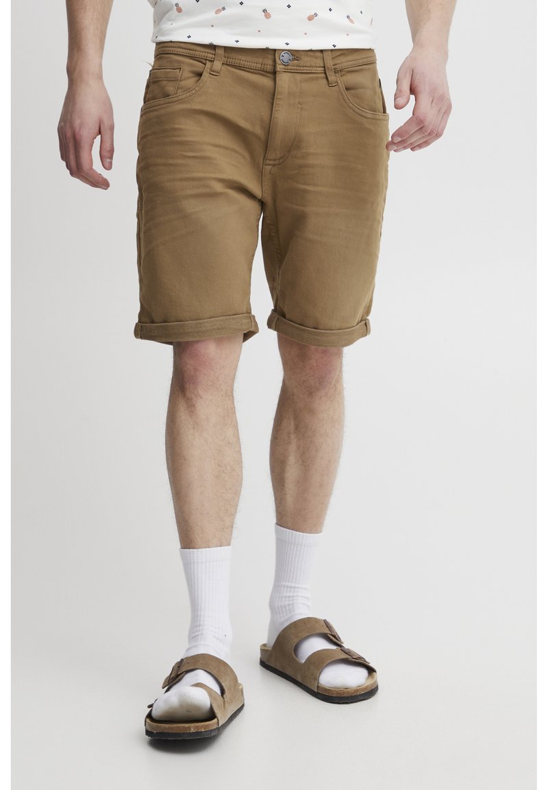 Beige Denim-Shorts mit umgeschlagenen Säumen, fünf Taschen und vorderem Knopfverschluss, kombiniert mit weißen Socken und braunen Sandalen. Minimalistisches Design.