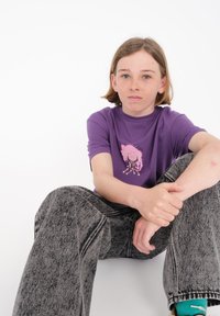 Camiseta de manga corta morada con diseño de medusas rosas, combinada con jeans de mezclilla grises de tiro alto, que presentan una textura desgastada y costuras visibles.