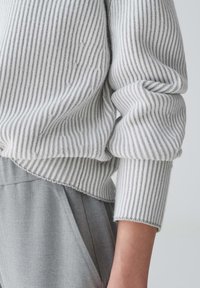 Grau gerippter Strickpullover mit kontrastierenden Streifen und umgeschlagenen Bündchen. Weiche Textur, leicht oversized Passform, kombiniert mit hellgrauen Hosen.