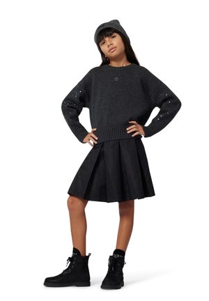 Pull en tricot gris avec un ourlet à côtes et des accents décoratifs, associé à une jupe plissée noire avec des motifs géométriques et des bottes à lacets noires.
