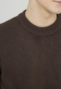 Pull en tricot marron avec un col rond côtelé. Vue en gros plan montrant la texture douce et les points réguliers.