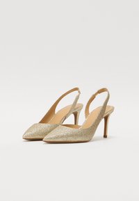 Sabots à talons hauts en paillettes dorées avec un bout pointu, un talon fin, et un dos ouvert, dotés d'un intérieur lisse et d'un dessus texturé.