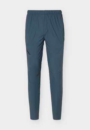 Pantalon de sport bleu pour homme, coupe slim, taille élastique, motif texturé subtil et logo noir sur la cuisse gauche.