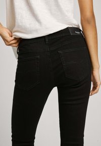 Svarta smala jeans med hög midja, med bakfickor och kontrasterande sömmar längs sömmarna, som visar en slät denimtextur.