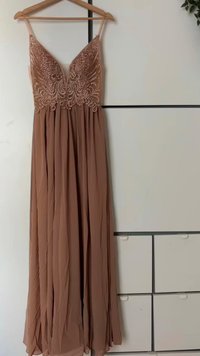 Rochie lungă, vaporousă, într-o nuanță moale de taupe, cu un bust brodat elegant, împodobit cu mărgele și curele subțiri. Prezintă un material pliat ce se extinde până la tiv.