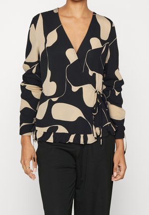 Femme portant un chemisier cache-cœur à motif abstrait noir et beige avec ourlet à volants et manches longues, assorti à un pantalon noir.
