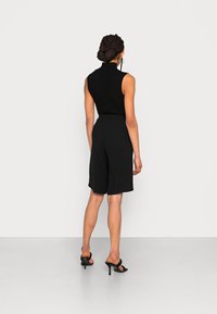 Top senza maniche a righe nere abbinato a pantaloni shorts neri a vita alta, in tessuto morbido, e sandali neri con tacco alto e punta aperta.