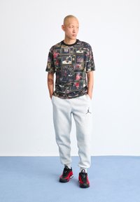 Grafisk t-skjorte med et flerfarget trykk av basketballscener. Grå joggebukser med svart logo. Svarte og røde sneakers fullfører antrekket.