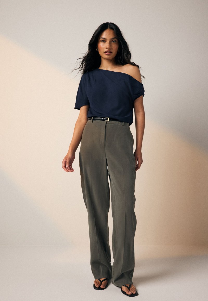 Navy off-shoulder top paired with high-waisted, loose-fitting olive trousers, and black flip-flops, featuring a subtle belt accent.