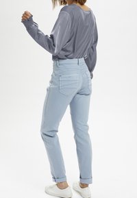 Lyseblå højtaljede jeans med en glat tekstur og oprullede manchetter, parret med en blød grå langærmet top med samlede ærmer.
