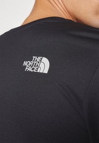 Sort t-shirt med korte ærmer lavet af glat, letvægtsstof, der har et hvidt logo fra "The North Face" på den øvre ryg.