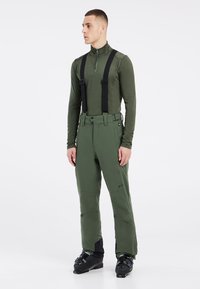 Groene skibroek met verstelbare zwarte bretels, ritszakken en versterkte onderbenen, gecombineerd met een bijpassend langarmshirt.