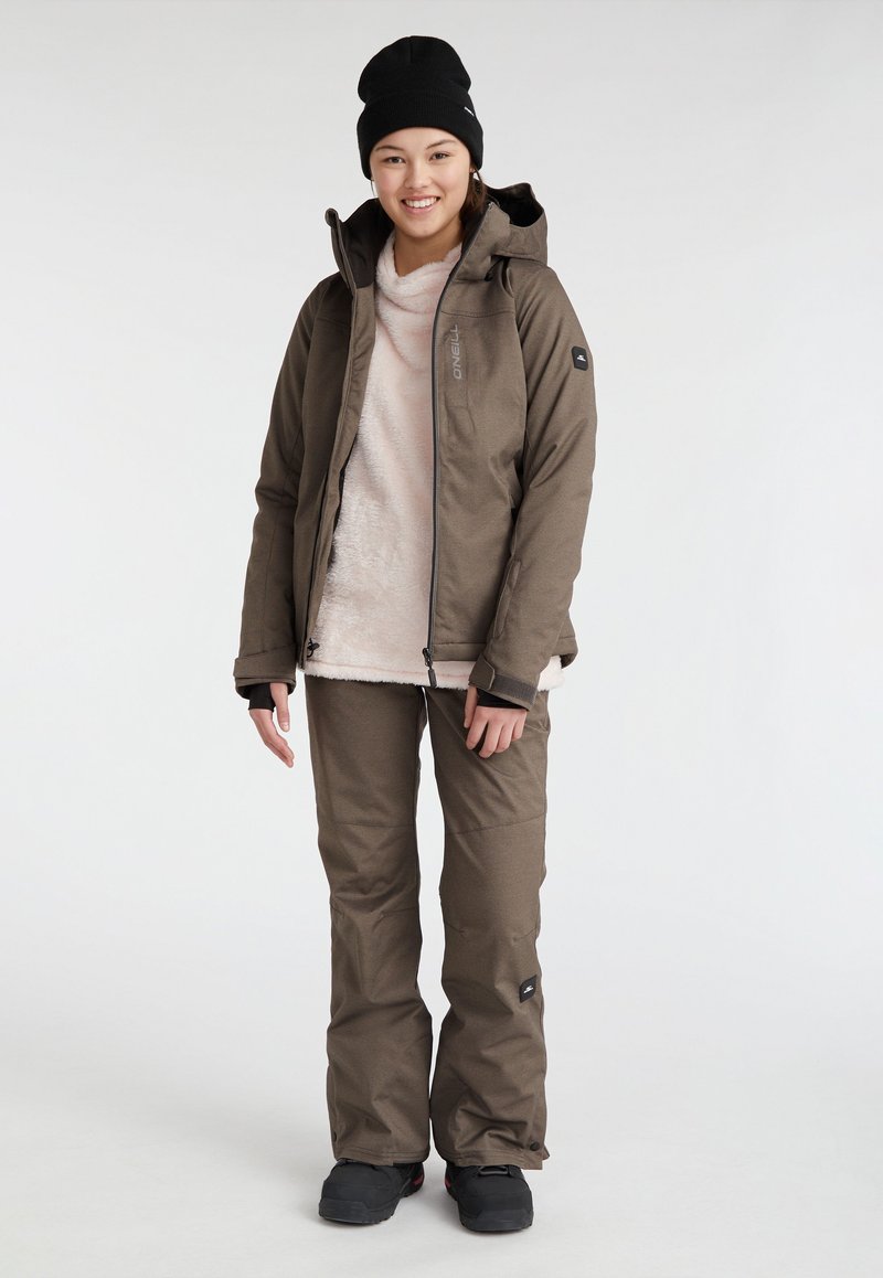 Braune, wetterfeste Jacke und passende Hose, die über einem leichten Fleece-Oberteil getragen werden. Zubehör umfasst eine schwarze Mütze und Fußbekleidung.