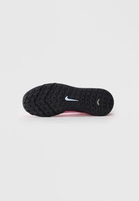 Svart gummisåle på en sportsko med mønstrede knopper og en liten hvit Nike-svush i midten, mot en enkel hvit bakgrunn.