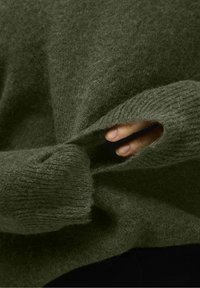 Maglione verde in lana con una consistenza morbida, caratterizzato da un dettaglio a taglio sul polsino. La vista ravvicinata rivela una vestibilità ampia e orlo a coste.