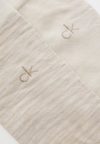 Calcetines de mezcla de algodón en beige claro, con un patrón de rayas texturizadas en un lado y punto liso en el otro, con un sutil logo "ck".