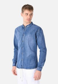 Camicia in denim di colore blu sfumato con colletto arrotondato, chiusura a bottoni, maniche lunghe e dettagli di cucitura in evidenza.