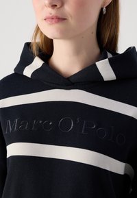 Sudadera con capucha azul marino con rayas horizontales blancas, que presenta un logo bordado. Tejido de algodón suave; incluye una capucha con cordón ajustable.