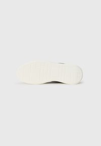 Talpa de sneaker neagră cu o talpă din cauciuc alb texturat. Are un model de pătrate și linii pentru aderență. Suprafață netedă cu o ușoară curbură.