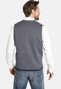 Strukturierte marineblaue Weste mit einem Rautenmuster, ausgestattet mit einem Rundhalsausschnitt und ärmellosem Design, kombiniert mit einem weißen Hemd und blauen Jeans.