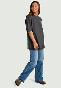 Mørkegrå oversized T-shirt med korte ærmer og en lomme, parret med lyseblå lige ben jeans og brune sko.