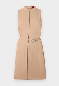 Μπεζ φόρεμα μέχρι το γόνατο χωρίς μανίκια, με ψηλό λαιμόκοψη, λεπτή μαύρη κάθετη γραμμή στο κέντρο και ζώνη που ταιριάζει με ασημένια οβάλ αγκράφα.