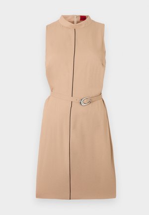 Ärmelloses, knielanges, beiges Kleid mit hohem Ausschnitt, dünner schwarzer vertikaler Linie in der Mitte und passendem Gürtel mit silberner ovaler Schnalle.
