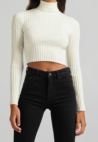 Vit ribbad polokrage tröja med långa ärmar, cropped design, kombinerad med högmidjade svarta jeans med en figursydd passform.