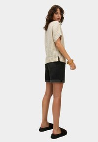 Top corto de manga corta a rayas claras en beige y blanco con un ajuste relajado, combinado con pantalones cortos de mezclilla oscuros y sandalias planas negras.