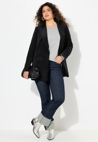 Blazer de pana negra, top gris, vaqueros de denim oscuro con dobladillo, y botas de tobillo plateadas. Los accesorios incluyen un clutch negro y una pulsera.
