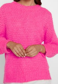 Pull en tricot rose vif avec une finition texturée, encolure ronde et manches longues. Les détails des poignets sont légèrement surdimensionnés.