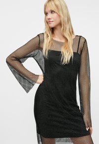 Fekete ruha hosszú, hálós ujjakkal, amelyeken gyémánt mintázat található. A test része testhez simuló, míg az ujjak harang alakúak.