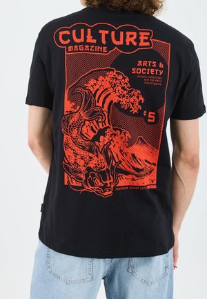 Personne portant un T-shirt noir avec un motif rouge représentant un poisson koi, des vagues, une montagne et un texte sur un magazine culturel et la culture visuelle japonaise.