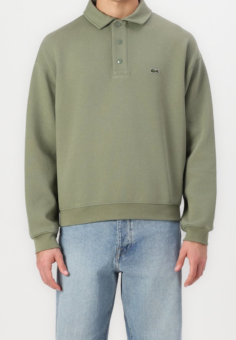 Zielona bawełniana bluza z kołnierzykiem polo, z zapięciem na trzy guziki, ściągaczami na mankietach oraz małym logo Lacoste na piersi.