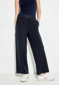Granatowe spodnie o szerokich nogawkach z teksturowanym pasem w haftem "POZTYWNOŚĆ" oraz kieszeniami po bokach, w połączeniu z białymi trampkami.