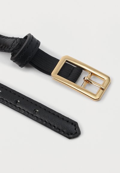 Μαύρη δερμάτινη ζώνη με χρυσή ορθογώνια αγκράφα και λεπτομέρεια από μαύρο ελαστικό λουράκι σε λευκό φόντο.