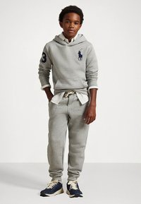 Sweatshirt com capuz cinzento de algodão com um grande logótipo azul-marinho e cordão, combinado com calças jogger a condizer e ténis azul-marinho com detalhes em creme.